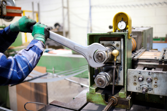 一个工厂维修工人用一个大扳手调整机器的图像。